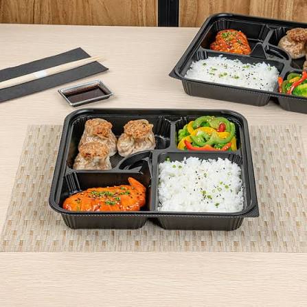 Black multi-compartment bento box packed with dumplings, rice, stir-fried vegetables and a chili glazed protein, served with chopsticks